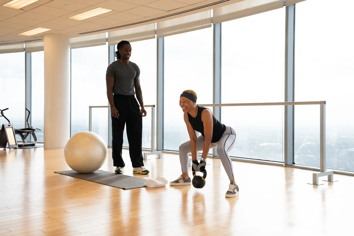 Chandler Thomas coaching a client through a kettlebell lift in a light-filled residential gym